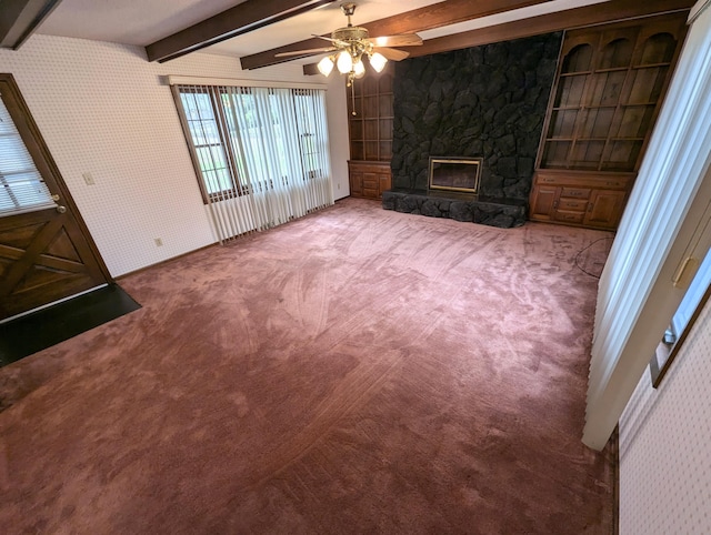 unfurnished living room with beam ceiling, a stone fireplace, ceiling fan, and carpet floors