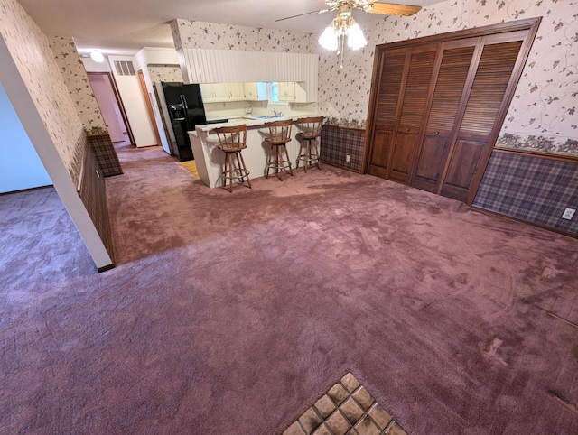 kitchen featuring kitchen peninsula, black refrigerator with ice dispenser, a breakfast bar, light colored carpet, and ceiling fan