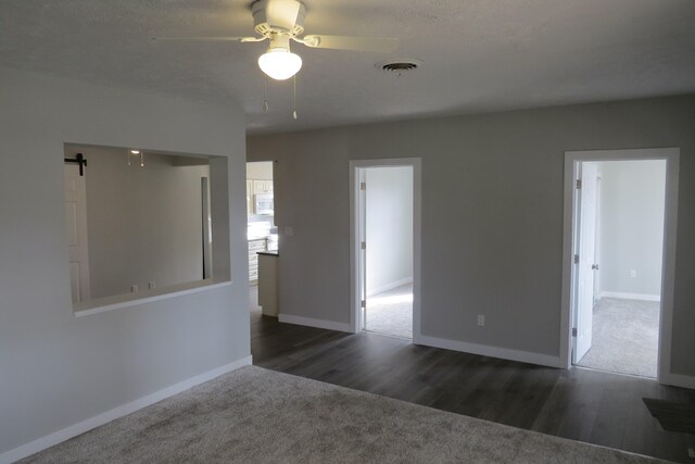 empty room featuring dark hardwood / wood-style flooring, a barn door, a textured ceiling, and ceiling fan