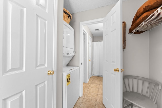 clothes washing area featuring light tile patterned flooring, stacked washing maching and dryer, and a textured ceiling