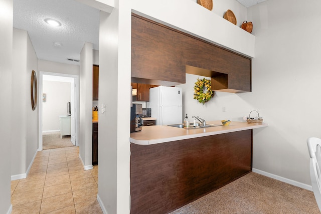 kitchen featuring a textured ceiling, white refrigerator, light colored carpet, and sink