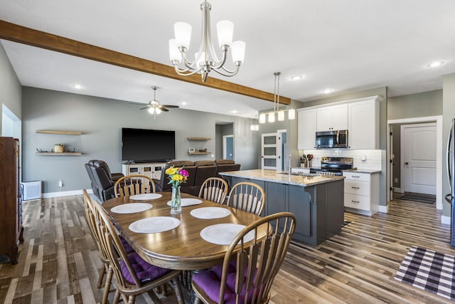 dining room with hardwood / wood-style floors, ceiling fan with notable chandelier, sink, and beamed ceiling