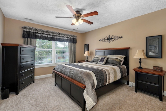 bedroom featuring a textured ceiling, light colored carpet, and ceiling fan