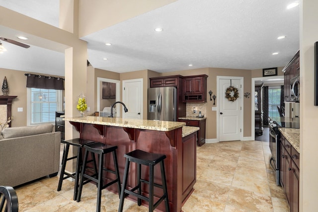 kitchen with stainless steel appliances, light stone counters, backsplash, a textured ceiling, and a breakfast bar