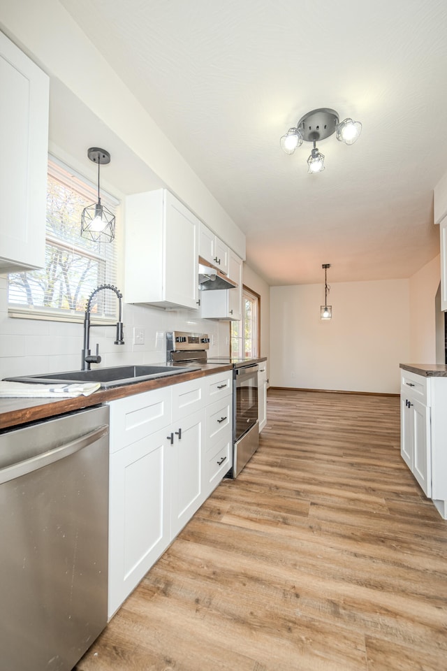 kitchen featuring decorative light fixtures, light wood-type flooring, stainless steel appliances, and white cabinetry