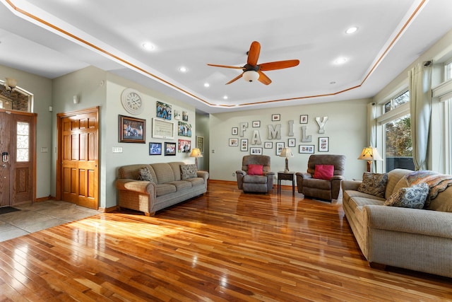 living room featuring ceiling fan, a tray ceiling, and light hardwood / wood-style flooring