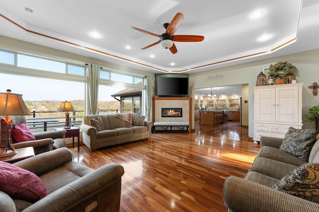 living room featuring a tray ceiling, ceiling fan with notable chandelier, and hardwood / wood-style flooring