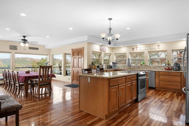 kitchen with dark wood-type flooring, light stone counters, pendant lighting, ceiling fan with notable chandelier, and appliances with stainless steel finishes