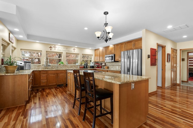 kitchen with appliances with stainless steel finishes, backsplash, decorative light fixtures, dark hardwood / wood-style floors, and a breakfast bar area