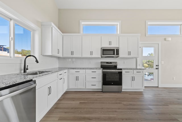 kitchen featuring white cabinets, sink, light hardwood / wood-style flooring, appliances with stainless steel finishes, and light stone counters