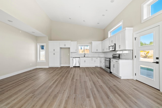 kitchen with appliances with stainless steel finishes, high vaulted ceiling, light hardwood / wood-style floors, and white cabinetry