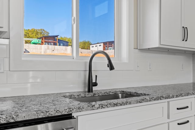 room details featuring white cabinetry, sink, light stone counters, stainless steel dishwasher, and backsplash