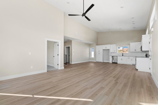 unfurnished living room featuring ceiling fan, light wood-type flooring, sink, and high vaulted ceiling