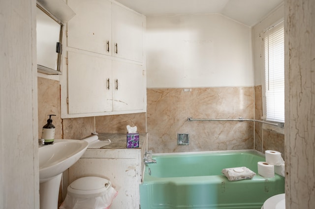 bathroom featuring tile walls, a bath, vaulted ceiling, and toilet