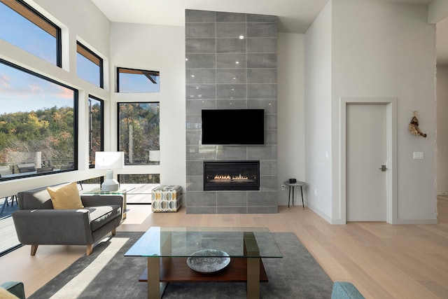 living room featuring wood-type flooring, a towering ceiling, and a tiled fireplace