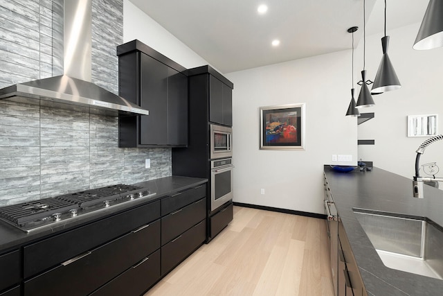 kitchen with decorative backsplash, stainless steel appliances, wall chimney range hood, decorative light fixtures, and light hardwood / wood-style floors