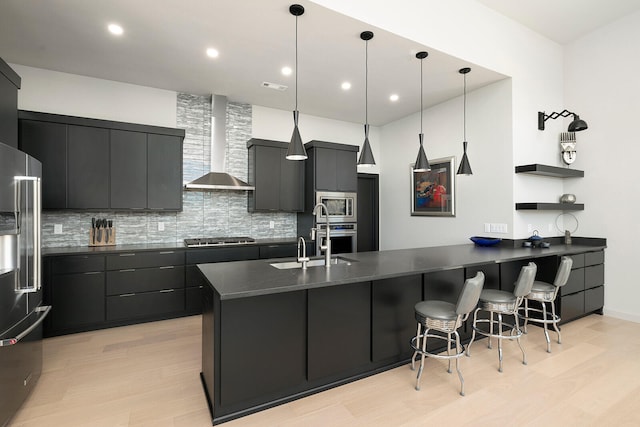 kitchen with backsplash, hanging light fixtures, wall chimney exhaust hood, a kitchen bar, and stainless steel appliances