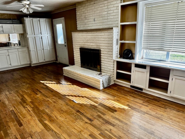 unfurnished living room with a brick fireplace, ornamental molding, a textured ceiling, ceiling fan, and light hardwood / wood-style flooring