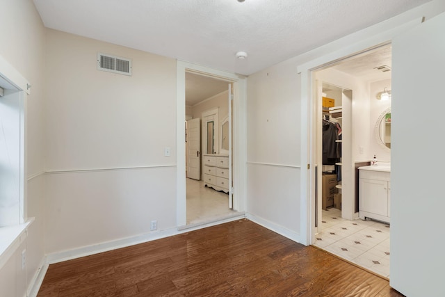 interior space with a walk in closet, ensuite bath, a textured ceiling, light hardwood / wood-style floors, and a closet