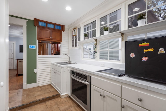 kitchen with ornamental molding, stainless steel oven, sink, white cabinets, and black stovetop