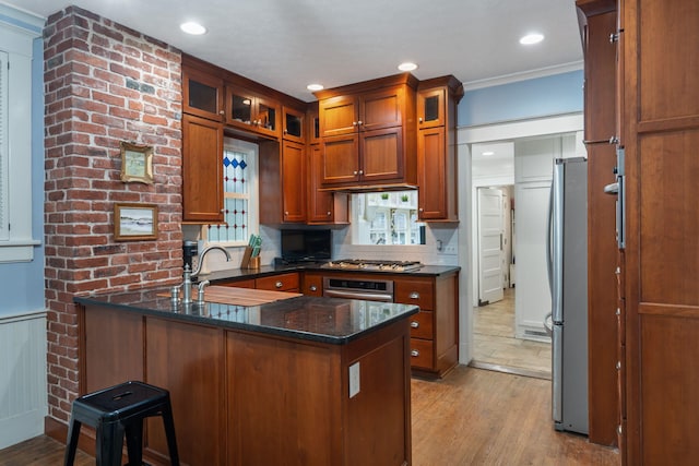 kitchen with sink, stainless steel appliances, kitchen peninsula, dark stone countertops, and light wood-type flooring