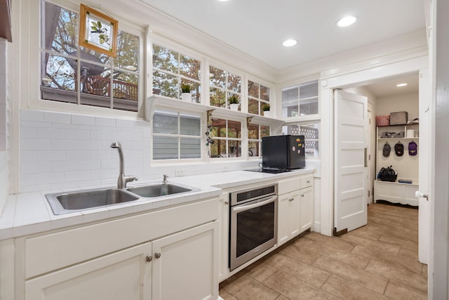 kitchen with backsplash, ornamental molding, sink, white cabinets, and oven