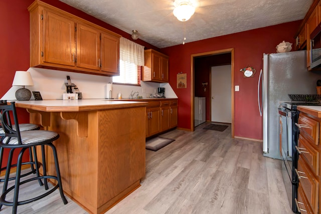 kitchen with black electric range, light wood-type flooring, a textured ceiling, a kitchen bar, and washer / clothes dryer