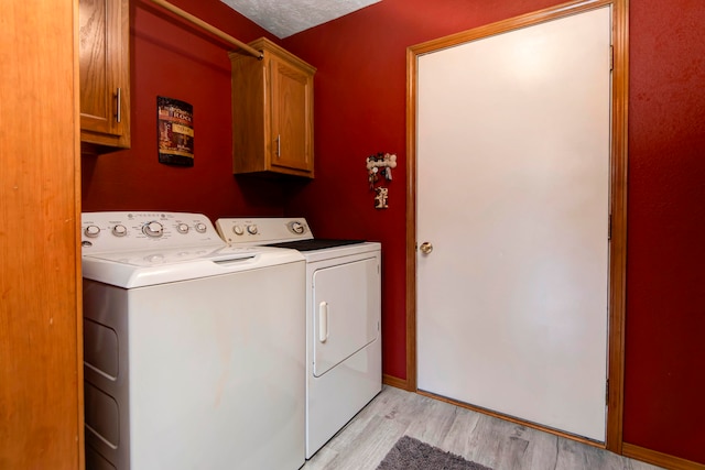 laundry area with washer and clothes dryer, cabinets, a textured ceiling, and light hardwood / wood-style floors