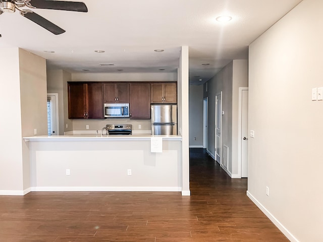 kitchen with kitchen peninsula, stainless steel appliances, a kitchen bar, and dark hardwood / wood-style floors