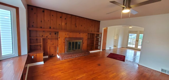 unfurnished living room with a wealth of natural light, wood-type flooring, wood walls, and a brick fireplace