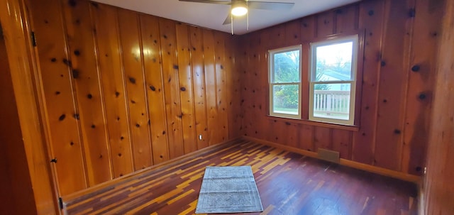 unfurnished room featuring ceiling fan, dark wood-type flooring, and wooden walls