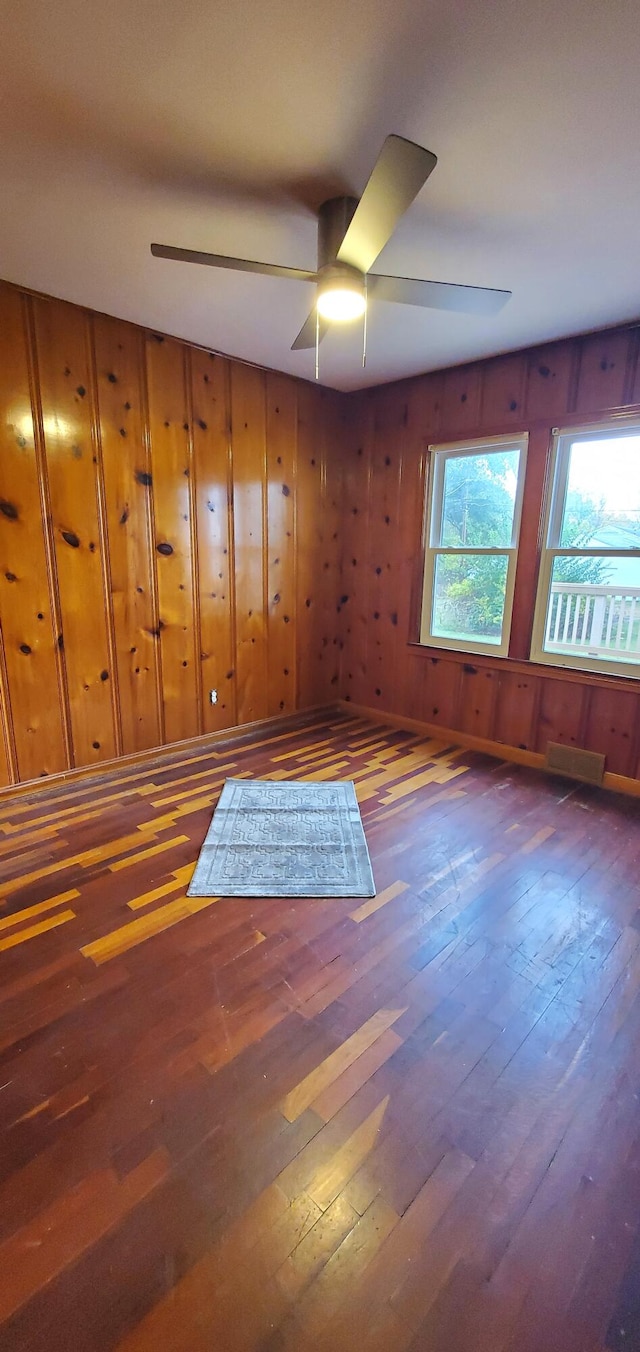 empty room with ceiling fan, dark wood-type flooring, and wood walls