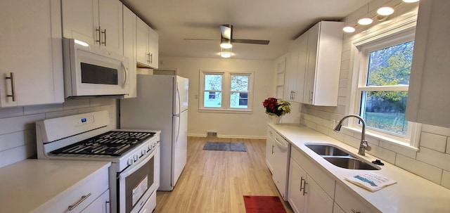 kitchen featuring a wealth of natural light, white cabinetry, sink, and white appliances