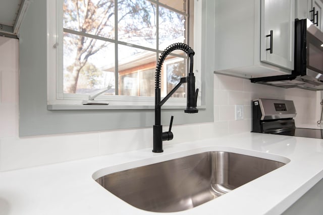 interior details with backsplash, sink, and stainless steel appliances