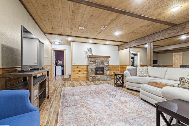 living room featuring light wood-type flooring, wooden walls, a stone fireplace, and wooden ceiling