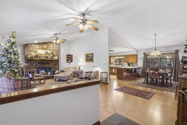 living room with ceiling fan, a fireplace, vaulted ceiling, and light wood-type flooring