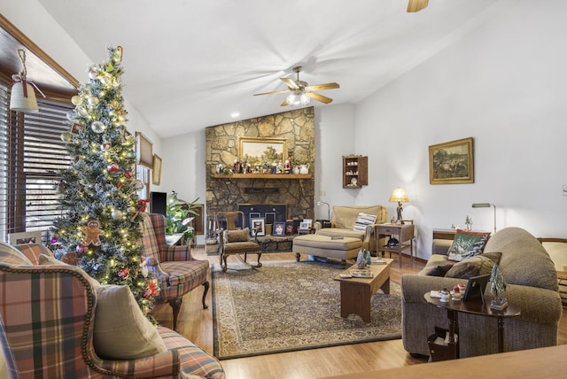 living room featuring hardwood / wood-style floors, ceiling fan, a stone fireplace, and lofted ceiling