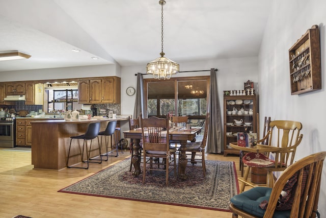 dining room with sink, an inviting chandelier, vaulted ceiling, and light hardwood / wood-style flooring