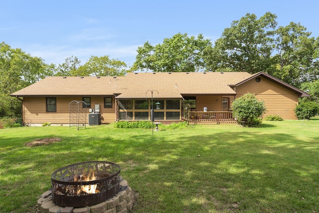 back of property featuring central AC unit, an outdoor fire pit, a lawn, and a sunroom