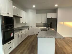 kitchen featuring dark wood-type flooring, black appliances, sink, an island with sink, and white cabinetry