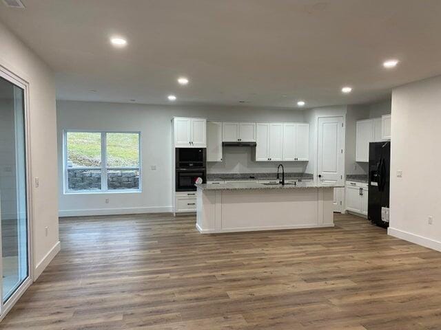 kitchen with a center island with sink, black appliances, sink, dark hardwood / wood-style flooring, and white cabinetry