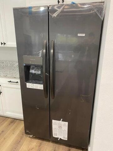 interior details featuring white cabinetry, refrigerator with ice dispenser, light stone counters, and light wood-type flooring