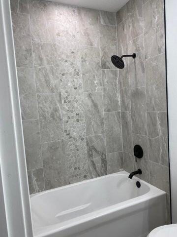 bathroom with toilet and tiled shower / bath