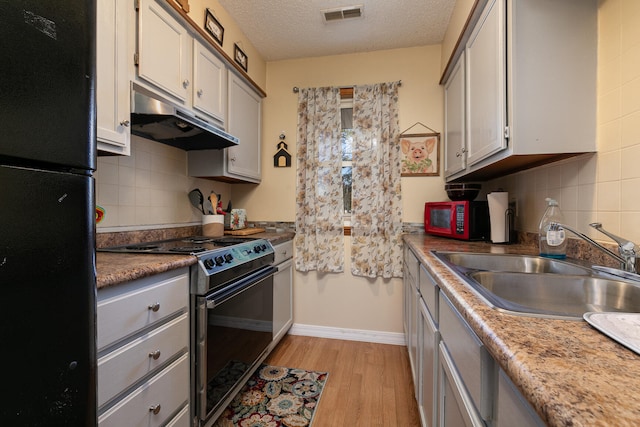 kitchen with backsplash, black appliances, sink, a textured ceiling, and light hardwood / wood-style floors