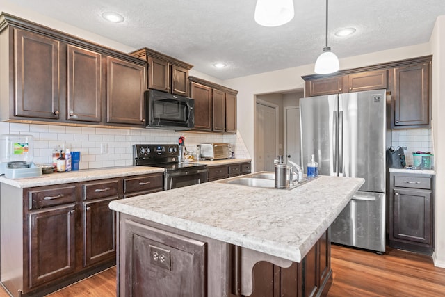 kitchen featuring decorative backsplash, dark hardwood / wood-style flooring, stainless steel appliances, hanging light fixtures, and an island with sink