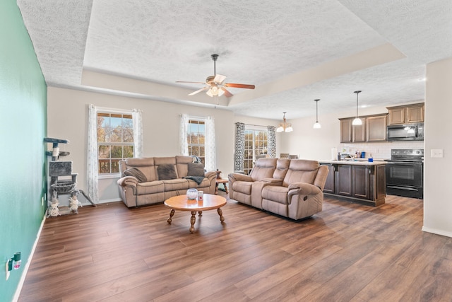 living room featuring dark hardwood / wood-style floors, ceiling fan, a textured ceiling, and a tray ceiling