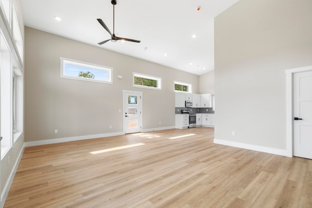 unfurnished living room with ceiling fan, a towering ceiling, and light hardwood / wood-style flooring