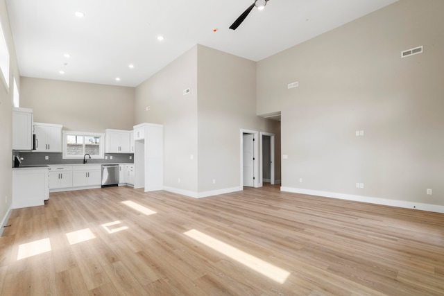 unfurnished living room with ceiling fan, sink, a high ceiling, and light hardwood / wood-style flooring