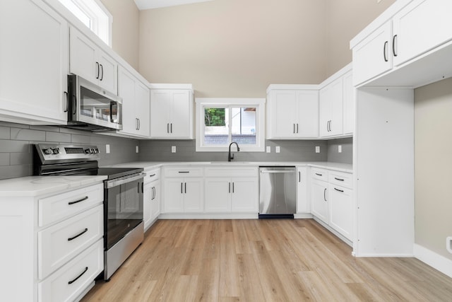 kitchen featuring decorative backsplash, appliances with stainless steel finishes, sink, light hardwood / wood-style floors, and white cabinetry