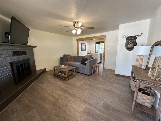 living room with a textured ceiling, ceiling fan, dark hardwood / wood-style floors, and a brick fireplace